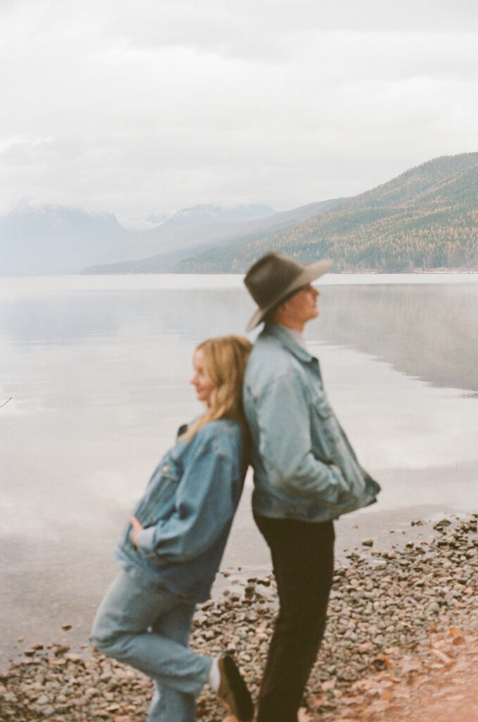 couple poses back to back beside lake