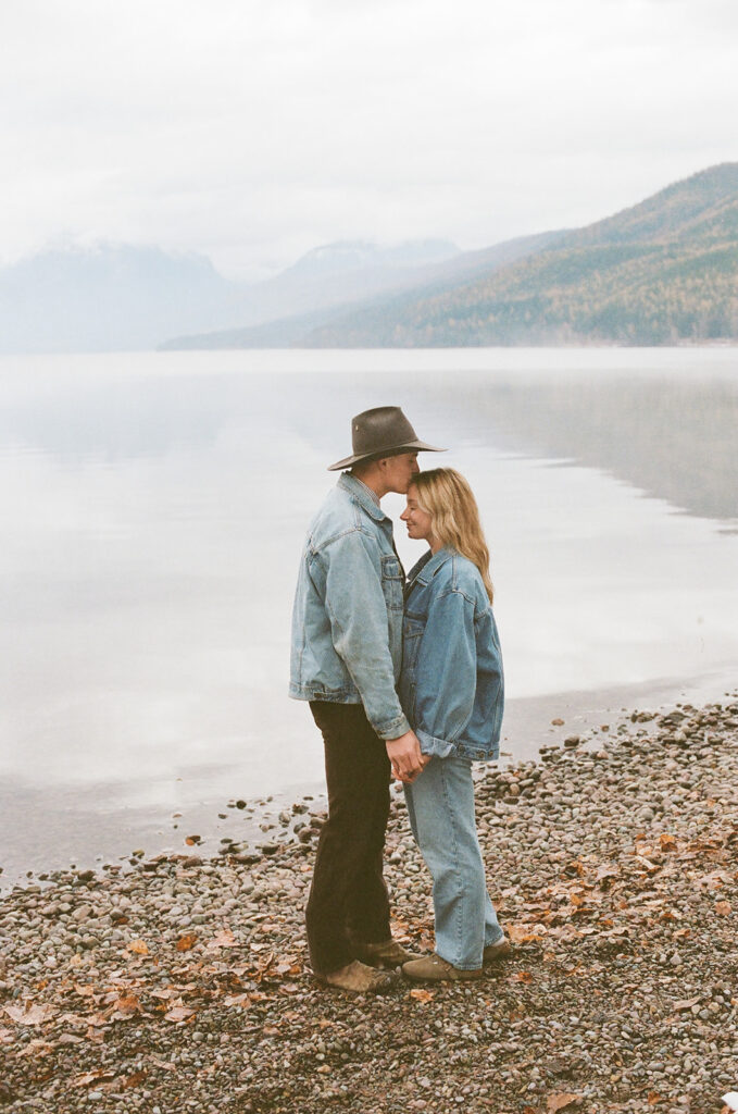 couple poses kisses beside Glacier National Park lake