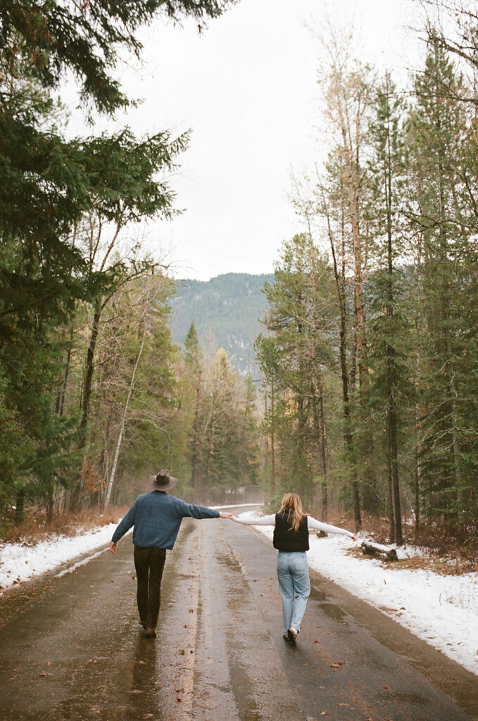 couple walks through snow-covered woods at Glacier National Park engagement