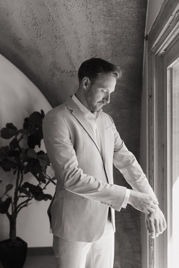 black and white photo. of groom fixing his sleeves