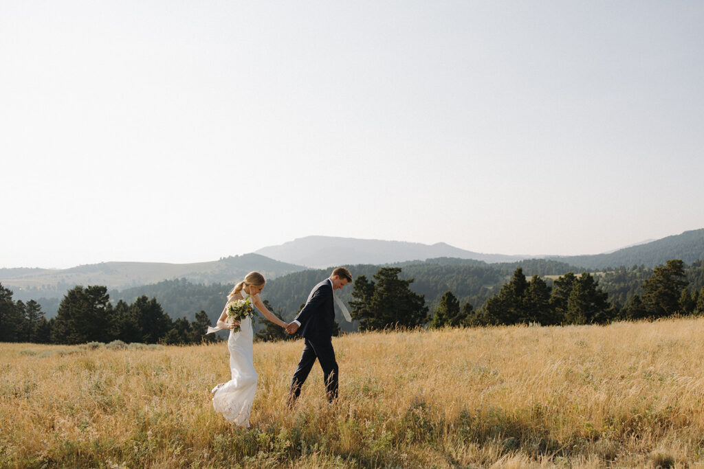 bride and groom walk through field at montana intimate wedding