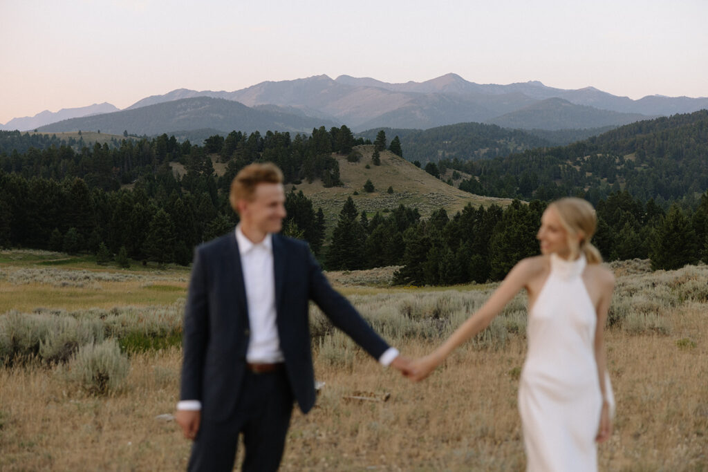 bride and groom walking through field on mountaintop