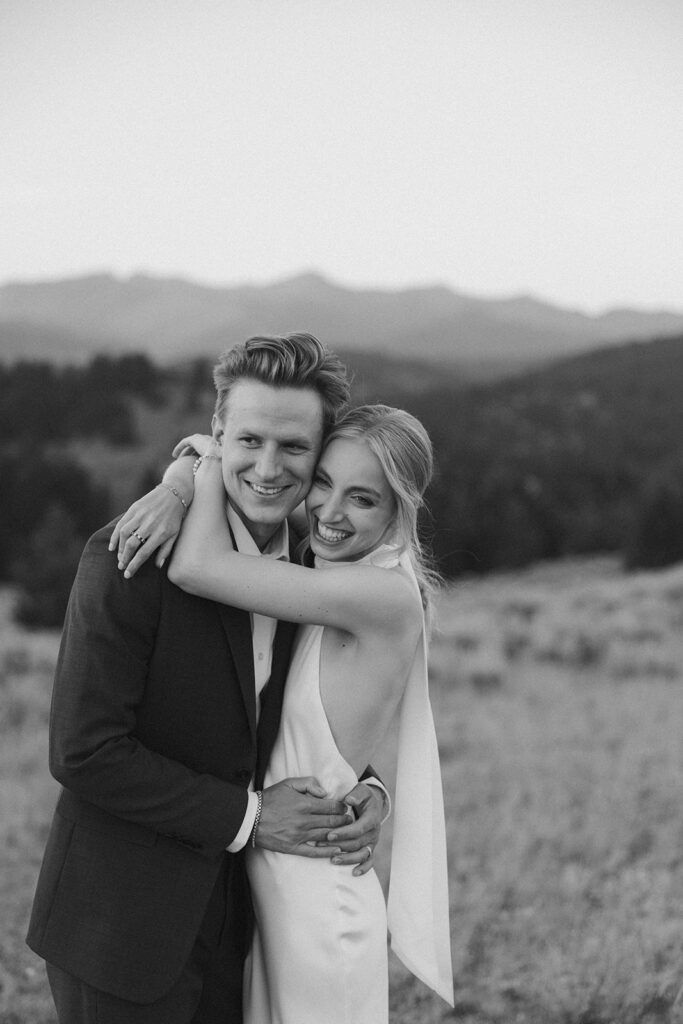 black and white of bride and groom hugging in field on mountaintop