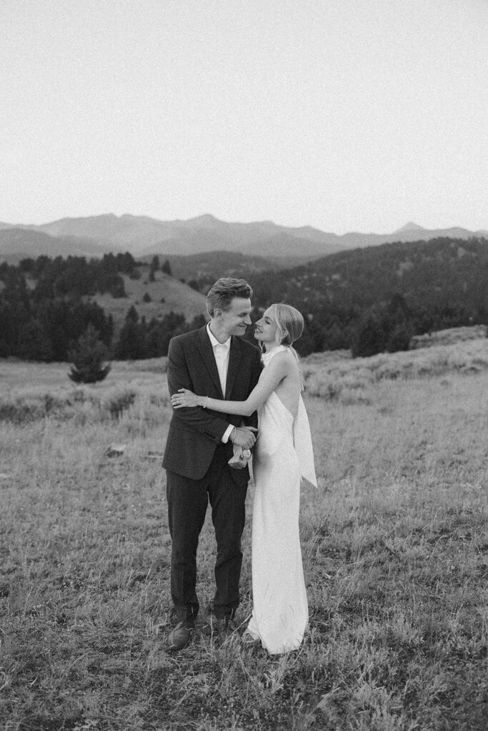 black and white of bride and groom walking through field on mountaintop