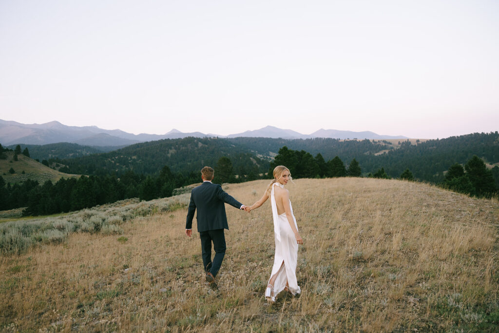 bride and groom walking through field on mountaintop