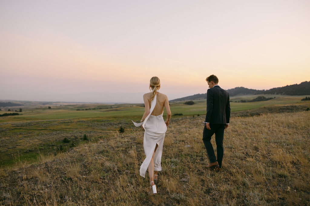 bride and groom walking through field on mountaintop