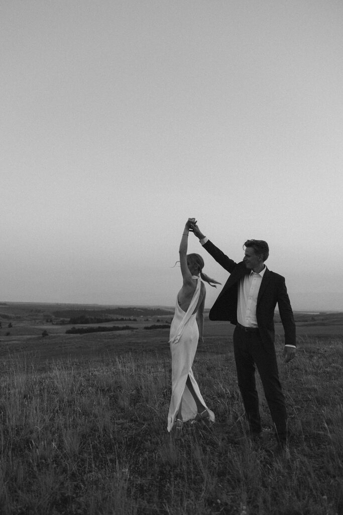 black and white of bride and groom twirling on mountaintop