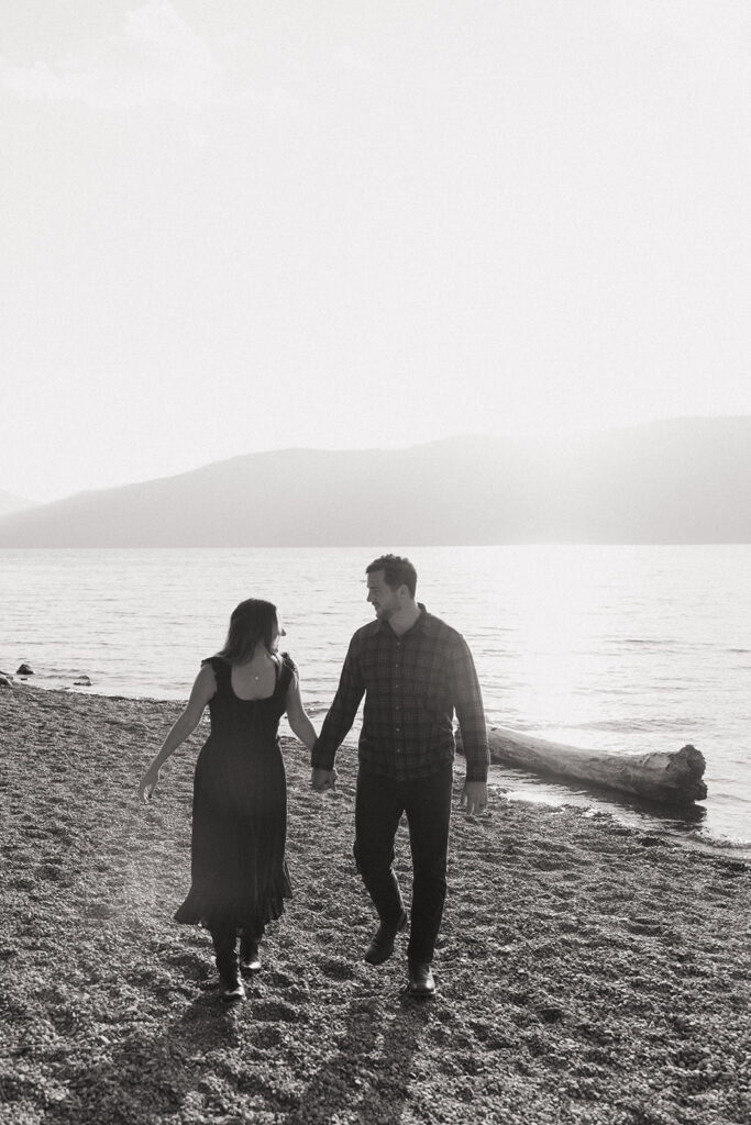 Couple holds hands and walks on the shore of Lake McDonald