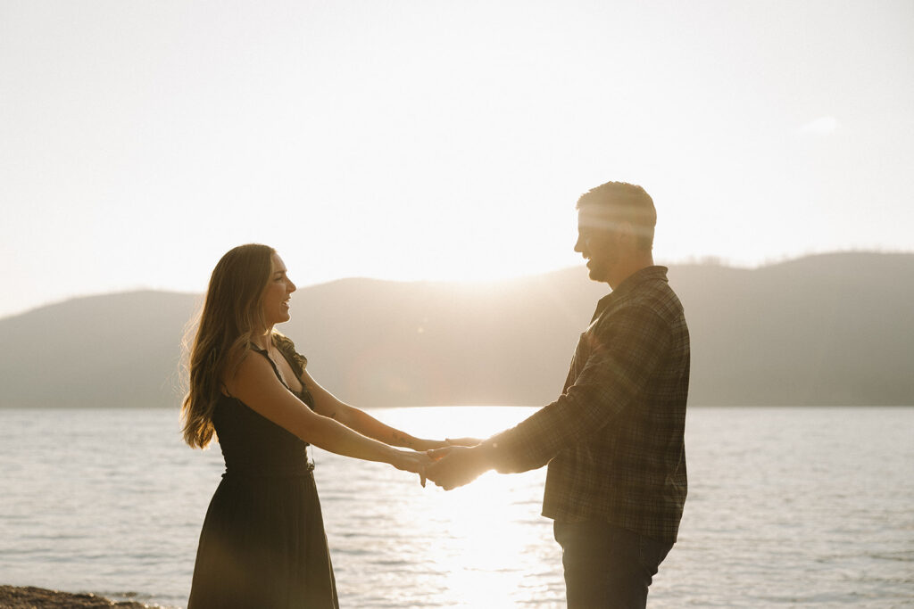 Couple holds hands with sunlight in the background at Lake McDonald