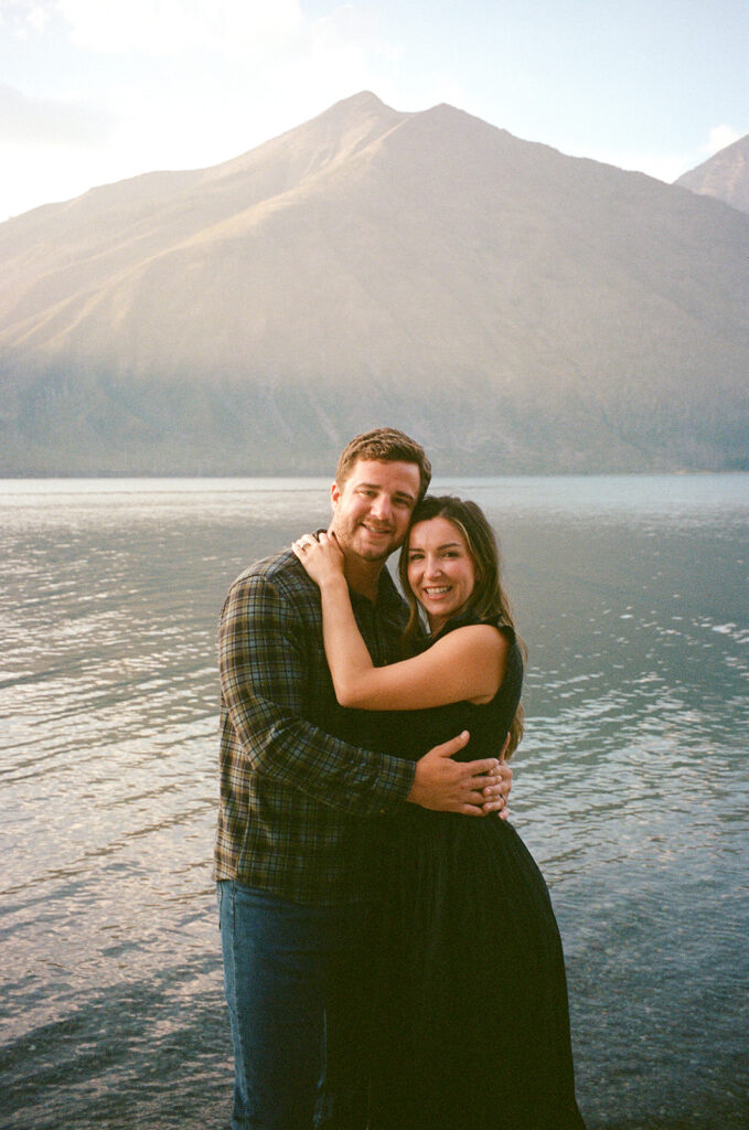 Couple stands and smiles next to Lake McDonald