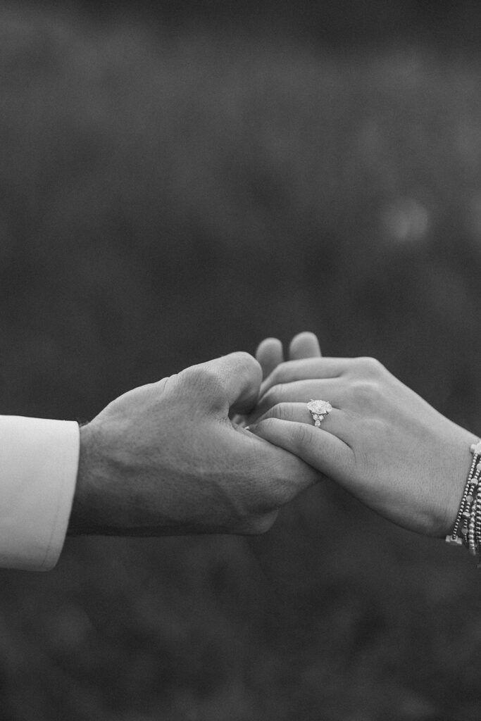 Black and white image of two hands showcasing the engagement ring