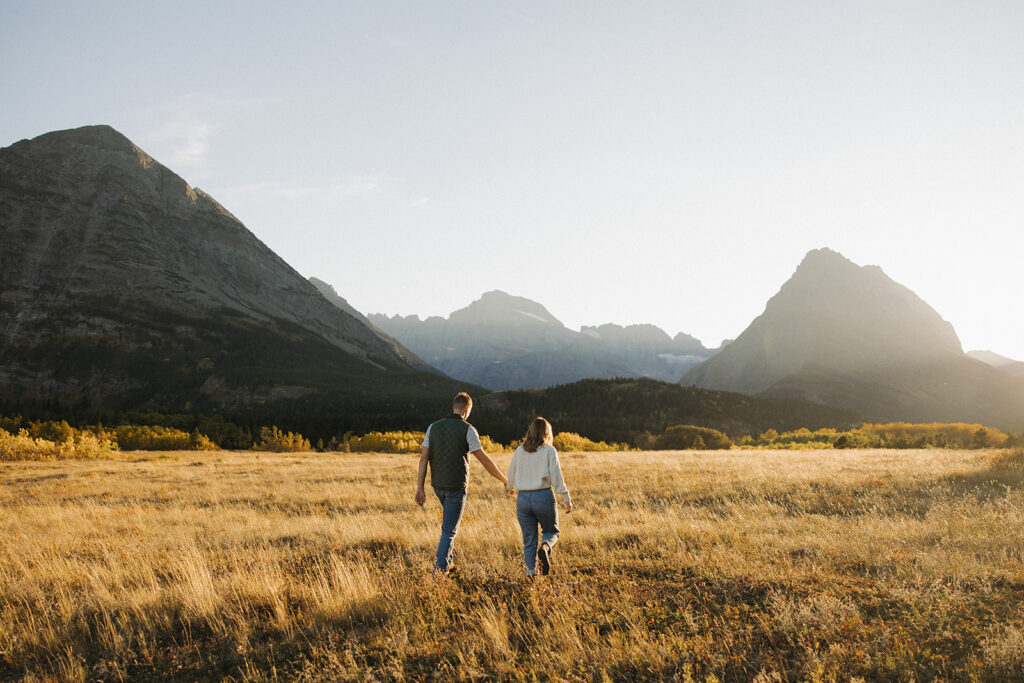 Couple walking in a field as the sun is setting in Glacier National Park