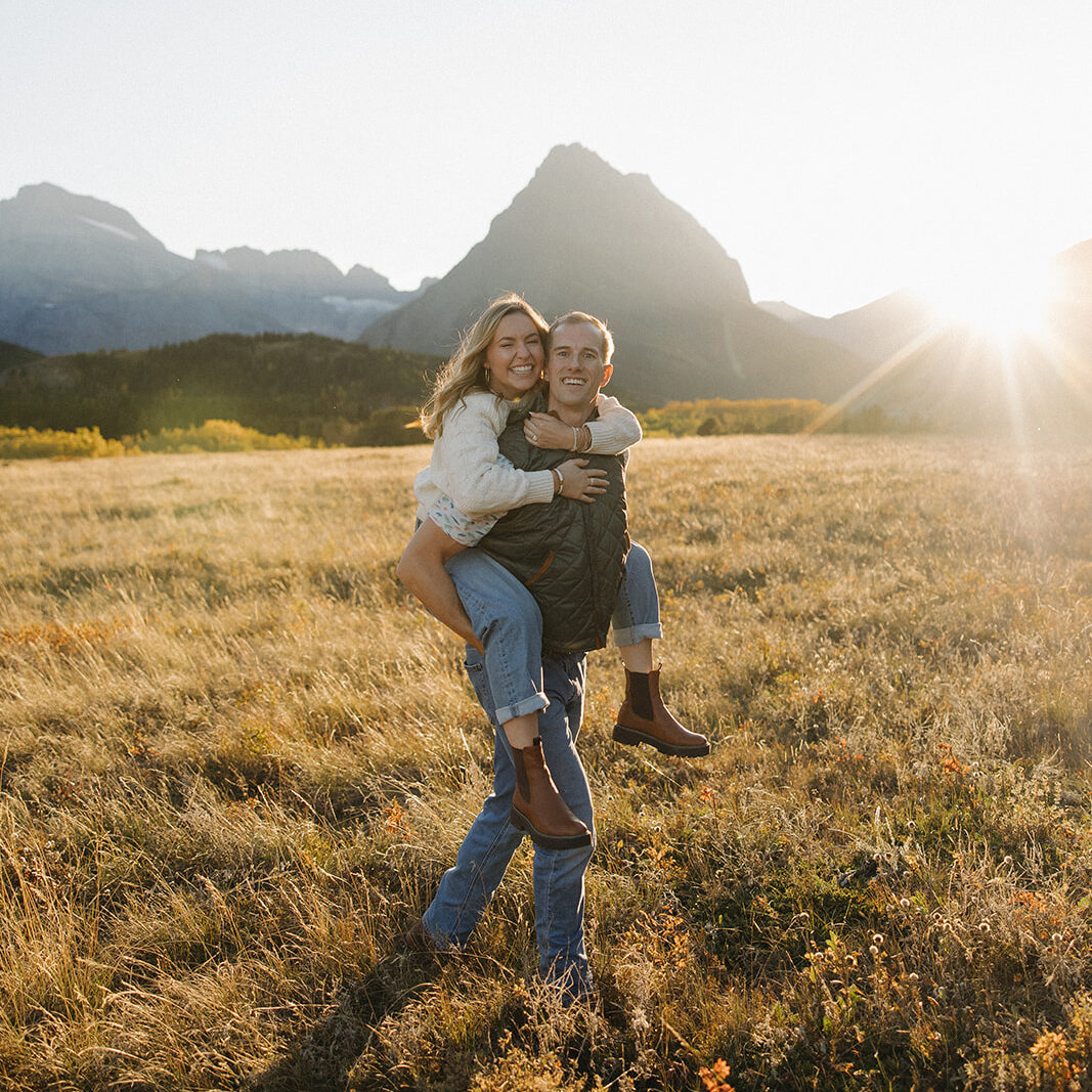 Couple smiling while in a piggyback pose in Glacier National Park